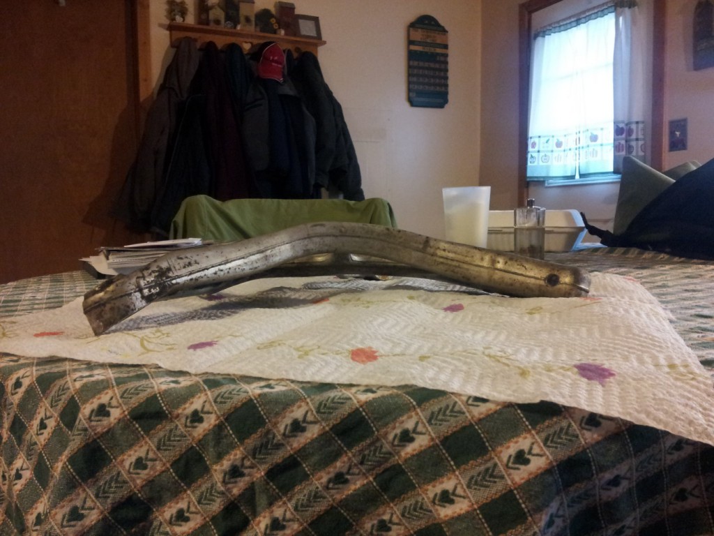Removed aluminum control arm lying on the kitchen table, seen end-on